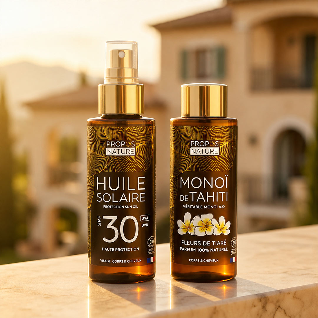 Two bottles of Propos Nature sun oil and Monoi de Tahiti on a table with a blurred outdoor background.