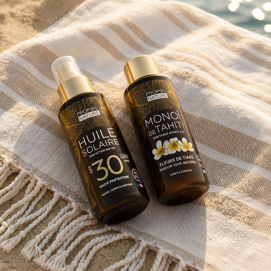 Two bottles of Propos Nature sun oil and monoi oil on a textured fabric surface.
