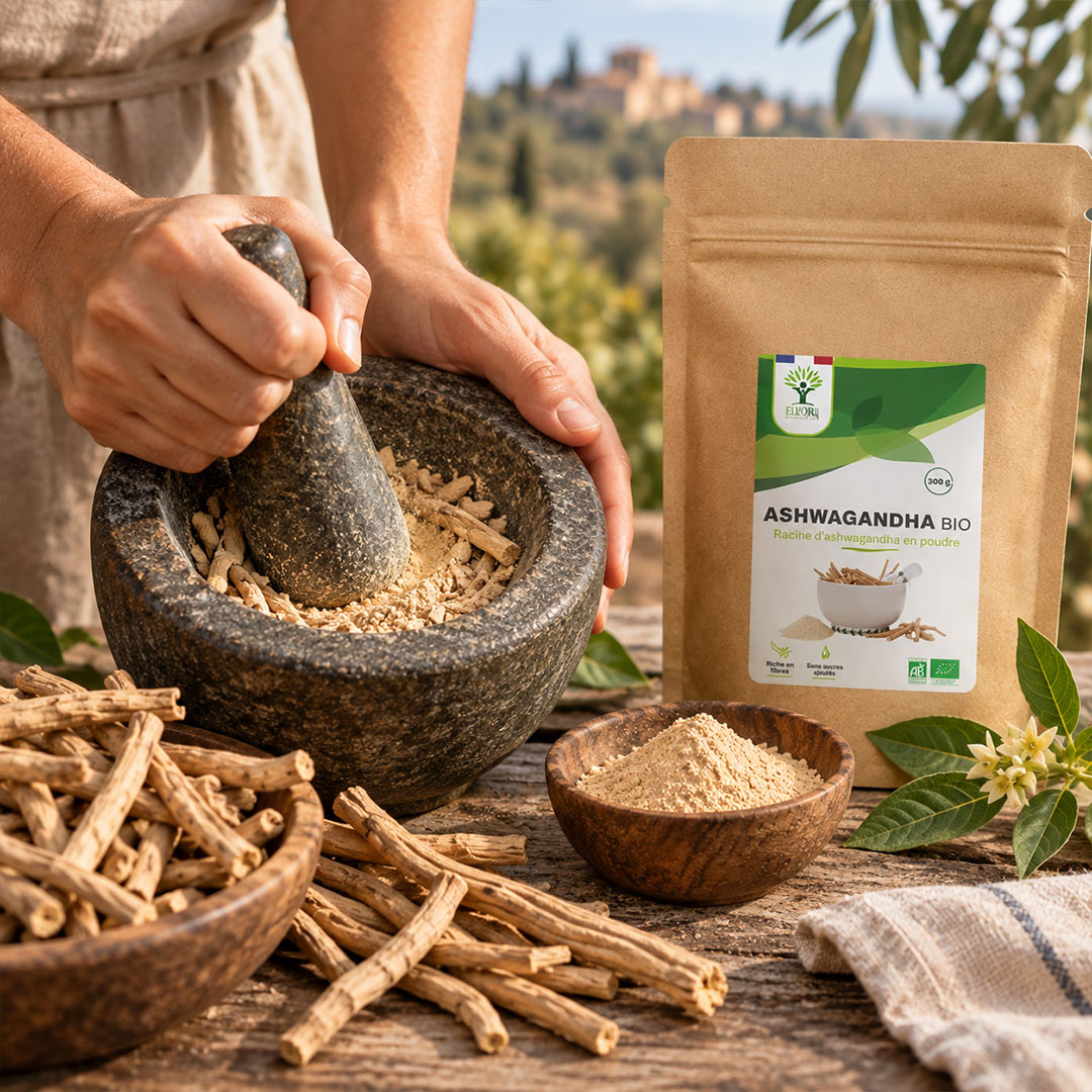 A person uses a stone mortar and pestle to grind dried roots beside a kraft pouch labeled Ashwagandha Bio, with bowls of powder and whole roots on a rustic table outdoors.
