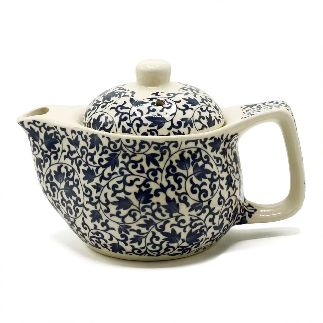 A ceramic teapot with a cream colored body and lid, decorated with an intricate navy blue floral and scroll pattern, shown on a white background.