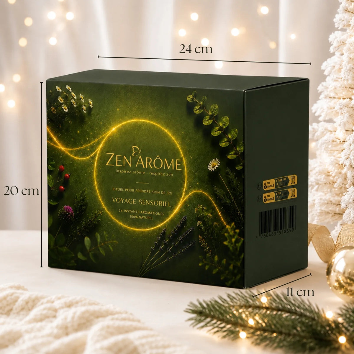 A dark green Zen Àrôme Advanets Calender box with botanical illustrations and a glowing yellow circular design, shown with dimension lines indicating 24 cm width, 20 cm height, and 11 cm depth. The box is styled on a white surface with warm bokeh lights, a white Christmas tree, and pine branches in the background.