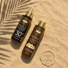 Two bottles of Propos Nature sunscreen on sand with a palm leaf shadow.