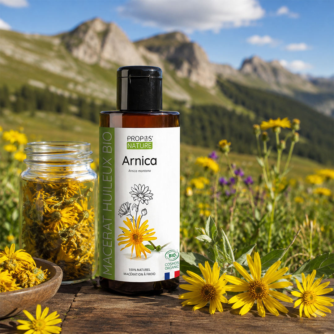 A bottle of Propos Nature Arnica botanical oil stands on a wooden surface outdoors, with a glass jar of dried yellow flowers beside it and mountain scenery in the background.