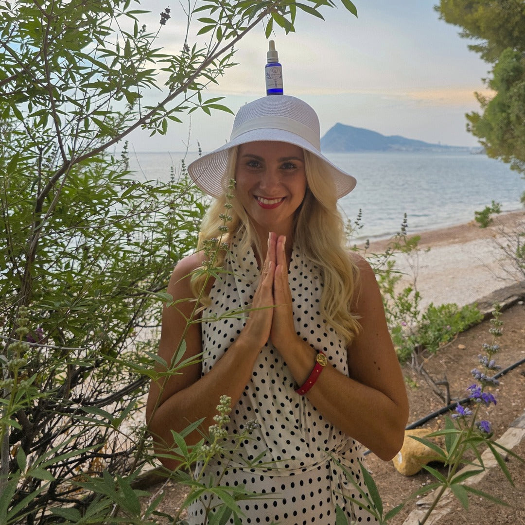 Woman in a polka dot dress and white hat by a scenic beach with mountains in the background.