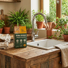 Kitchen sink with a bottle of cleaning product and potted plants on a wooden counter.