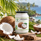 A jar of Bioptimal extra virgin organic coconut oil stands on a wooden surface outdoors, surrounded by coconuts, coconut pieces, and tropical palm leaves, with a blurred beach and ocean background.