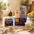 Complete Natural Dishwashing Starter Kit with ecological dish soap, dishwasher powder, reusable wooden dish brush and replacement head in a bright Mediterranean kitchen.