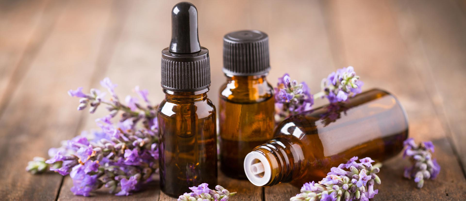 Lavender flowers laying on a dark wooden table with three amber glass bottles are standing in the middle
