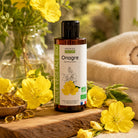 A bottle of Propos Nature Evening Primrose vegetable oil stands on a rustic wooden board surrounded by yellow flowers, with soft beige towels and greenery in the background.