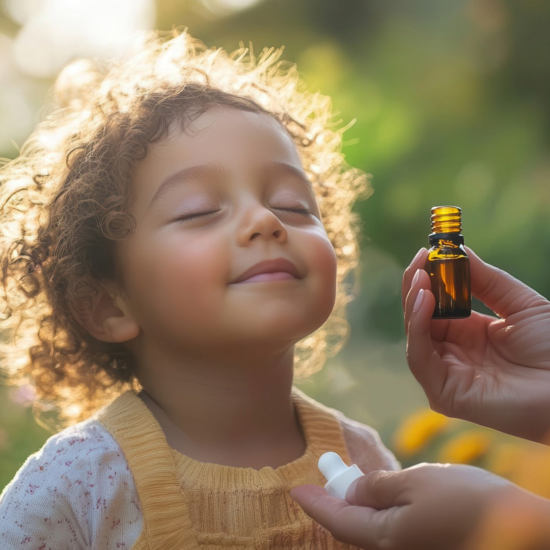 A child holding her head back with closed eyes and a smile, with adult hands holding an amber  bottle with oil