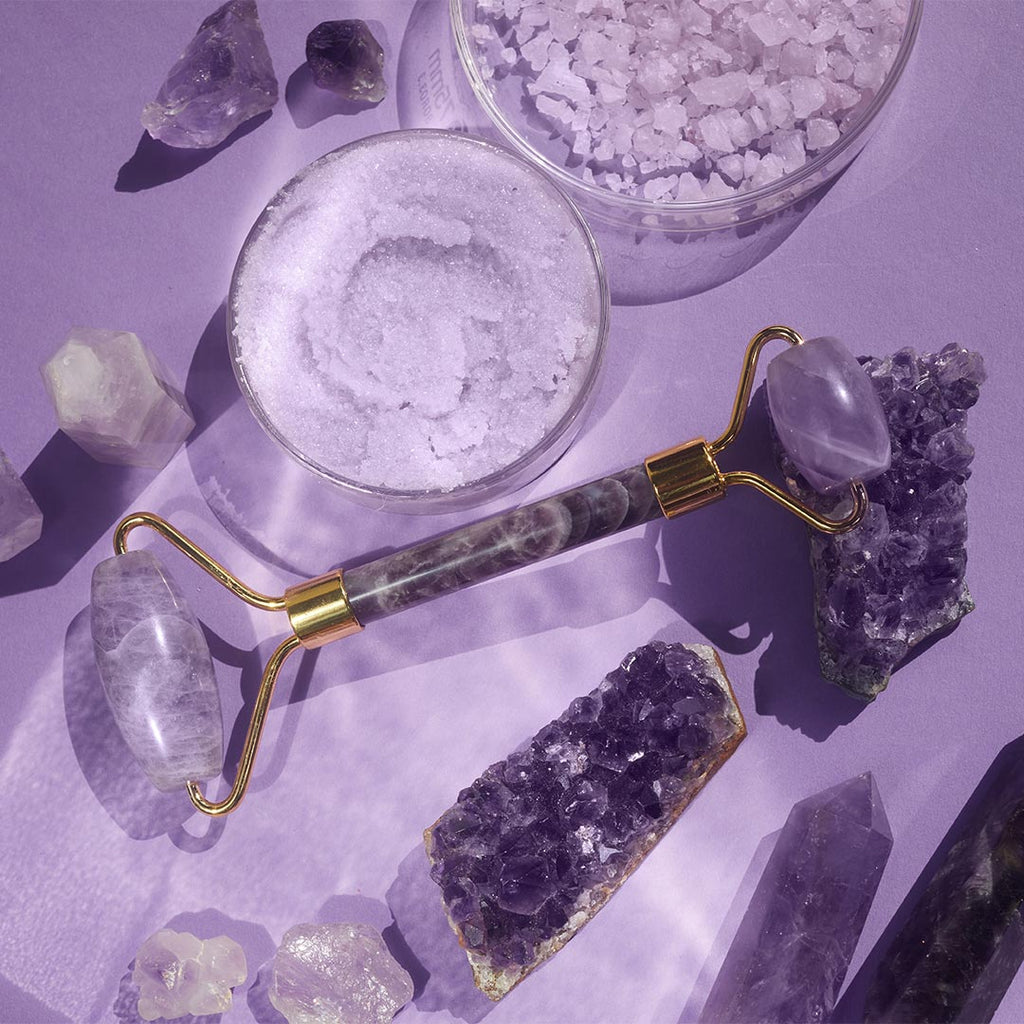 A Chi face roller Amethyst laying on a table on some Amethyst clusters, and other amathyst stones
