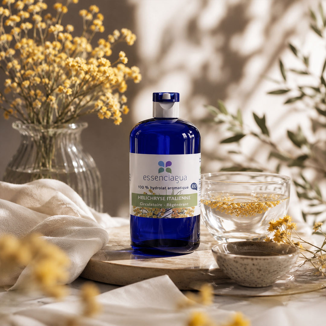 Blue bottle labeled 'essenciagua' on a table with flowers and a blurred background