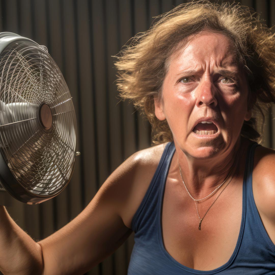 A woman with a fan in front of her, experiences a hot flash under menopause