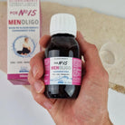 Hand holding a bottle of MenOligo supplement with its packaging in the background. Elliotti