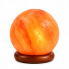 A glowing Himalayan salt Moon lamp with natural marbling, resting on a round dark brown wooden base against a plain white background.
