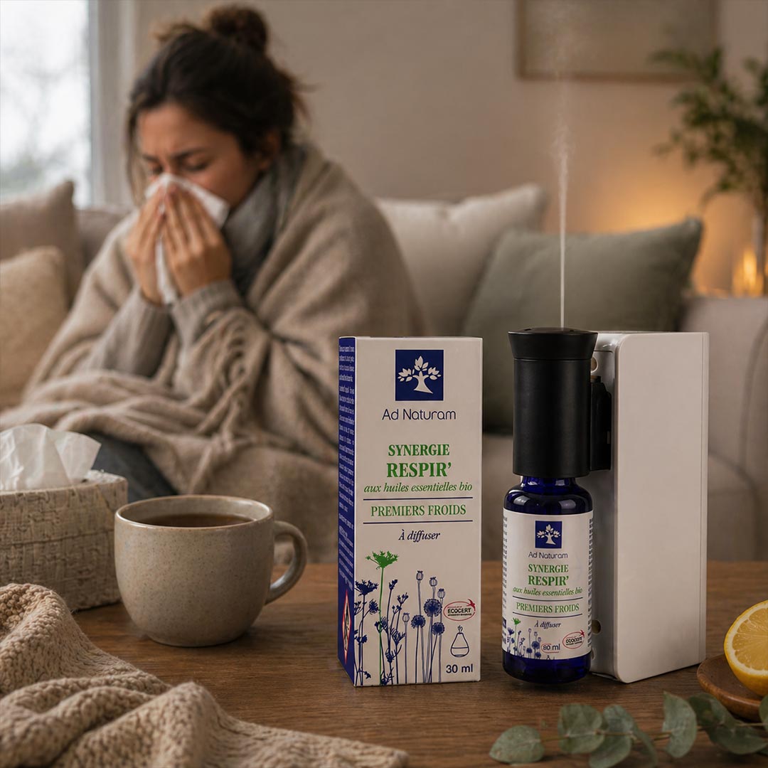 Woman with a cold sitting on a couch with a mug and tissues, next to Ad Naturam Synergie Respir product on a table.