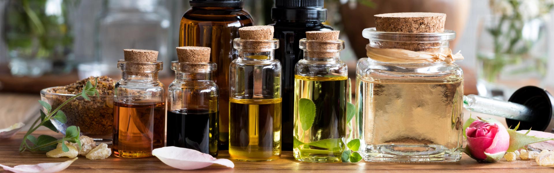 Essential oils in different glass bottles with herbs and rose petals