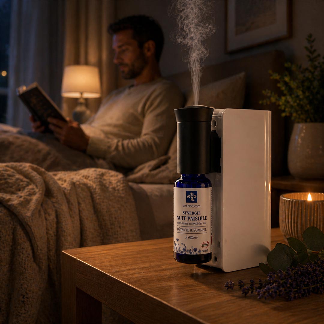 Person reading a book in a cozy room with an diffuser and bottle on a table.