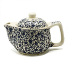 A ceramic teapot with a cream colored body and lid, decorated with an intricate navy blue floral and scroll pattern, shown on a white background.