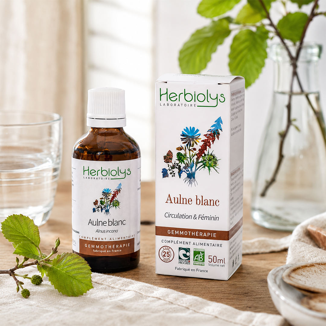 Herbiolys Laboratoires Aulne blanc dietary supplement, showing the amber glass bottle and its white box with botanical illustrations, styled on a wooden table with fresh green leaves and a glass of water.