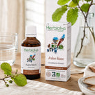 Herbiolys Laboratoires Aulne blanc dietary supplement, showing the amber glass bottle and its white box with botanical illustrations, styled on a wooden table with fresh green leaves and a glass of water.