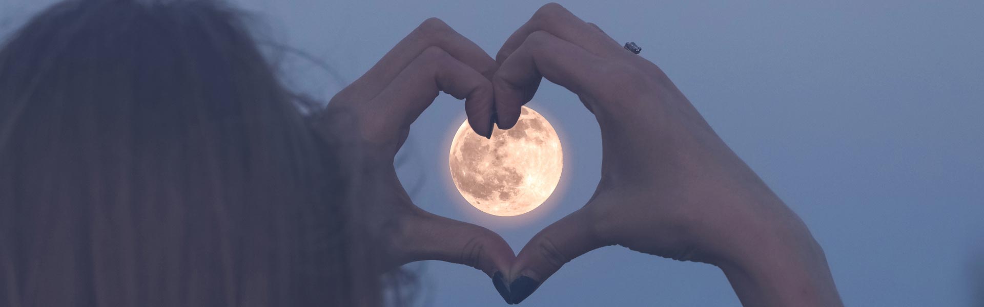 A woman forming her hands as a heart over the Moon