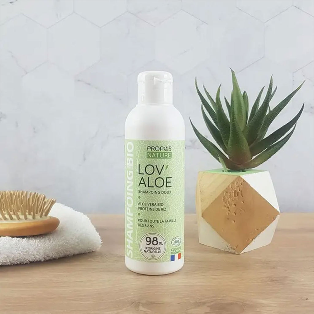 Propos nature Lov'Aloe  Shampo bottle  and a aloe vera plant and cloth with a hair brush on top of the cloth